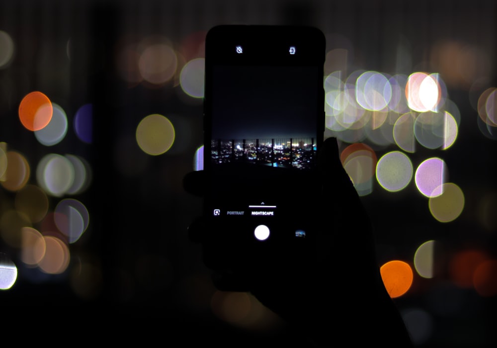 Tangan memegang ponsel pintar dengan cahaya bokeh di malam hari